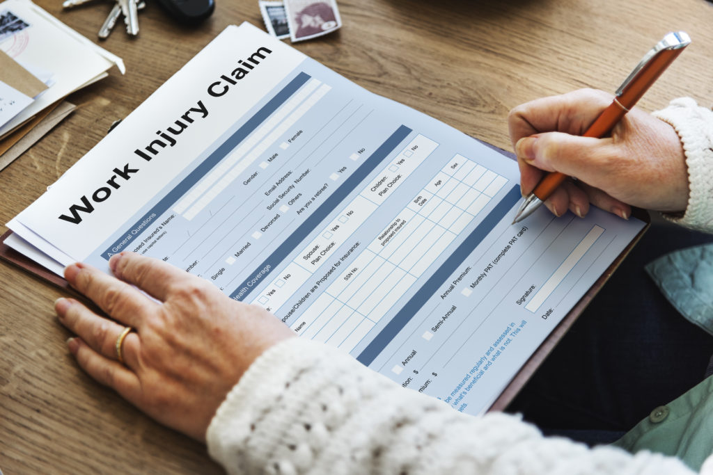 A person fills out a work injury claim form on a wooden desk
